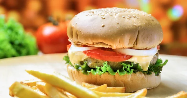 Burger on wooden plate with french fries and vegetables — Stock Photo, Image