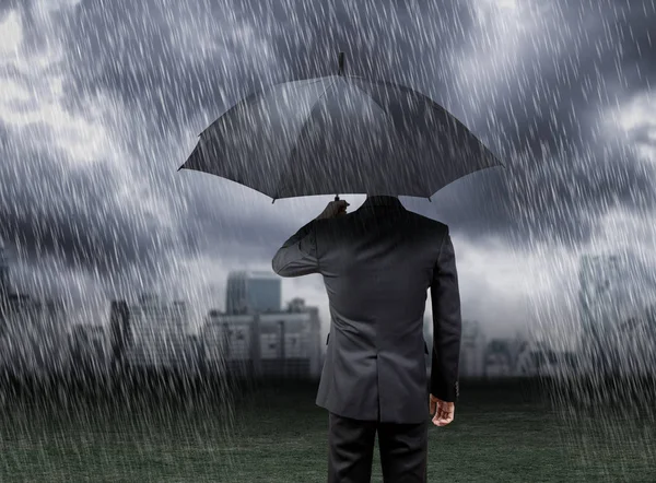Бизнесмен держит зонтик под дождём шторм с городским фоном — стоковое фото