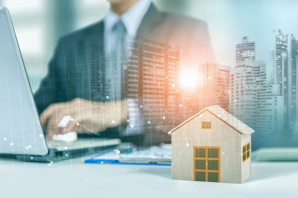 Hombre de negocios trabajar en el ordenador portátil con modelo de casa de madera, gráfico y la ciudad en el fondo de la noche — Foto de Stock