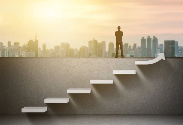 Businessman stand on rising arrow graph on staircase with city sunrise background — Stock Photo, Image