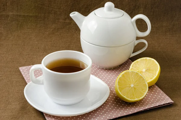 Na serwetki filiżankę herbaty z cytryną w spodek i czajnik — Zdjęcie stockowe