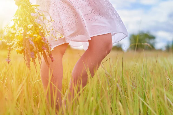 Glad modell flicka i vit klänning gå på fältet på solnedgång eller soluppgång med vildblommor. Frihet och renhet koncept — Stockfoto