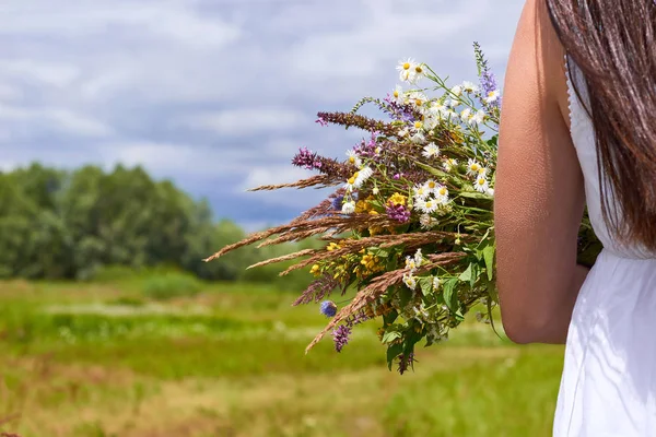 グリーン フィールドの手に野の花のブーケを持った白いドレスで幸せな女の子。自然と一体の概念 — ストック写真