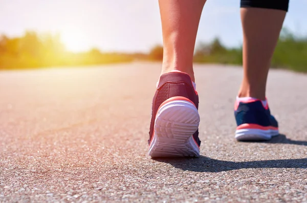 Jeune fille en chaussures de course court le long de la route, seules ses jambes sont visibles, jambes et baskets, lumière du soleil — Photo