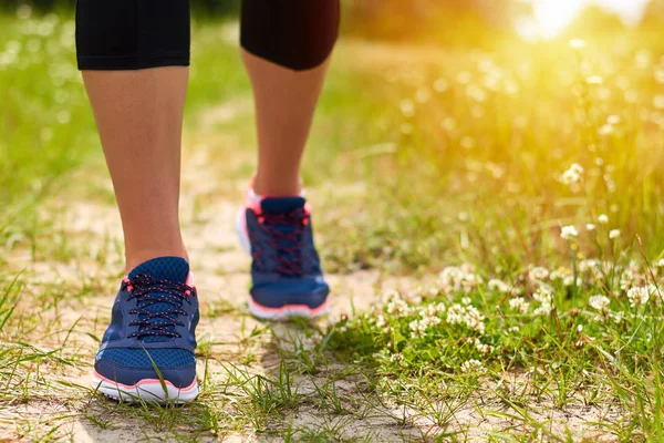 Fille est engagée dans des courses cardio à travers la forêt en baskets, seules les jambes sont visibles, les jambes et les baskets, la lumière du soleil — Photo