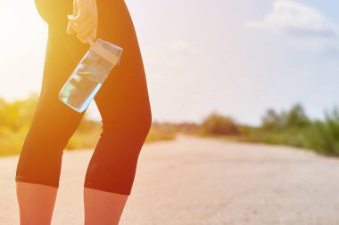Spor kız spor su şişesi ile yolda onun elinde duruyor. Spor yaşam tarzı, sağlık