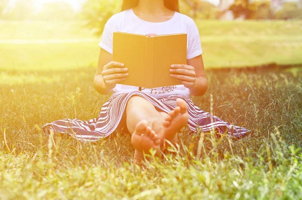 公園の芝の上に座って、本を読んでのスカートの少女。学習とレジャーの概念 — ストック写真