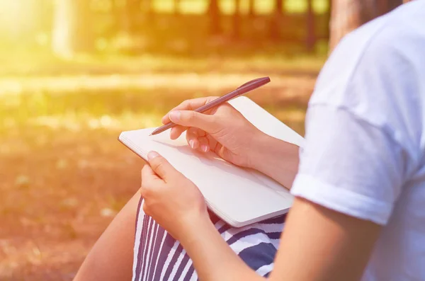 Schreibt das Mädchen in ein Notizbuch und studiert in der Natur. das Konzept von Freiheit und Einheit, Sonnenlicht — Stockfoto