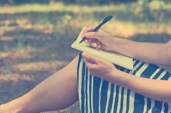 Schreibt das Mädchen in ein Notizbuch und studiert in der Natur. das Konzept der Freiheit und Einheit — Stockfoto