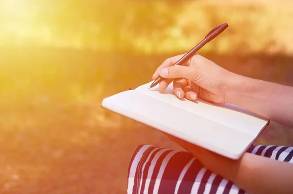 Une fille écrit sa main dans un cahier. Étudier et travailler dans le parc — Photo