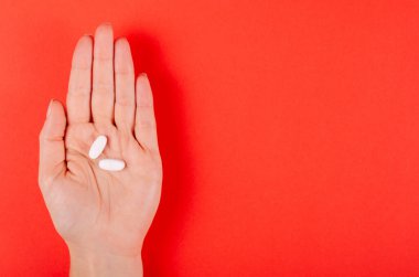 Kırmızı arka planda beyaz tıbbi haplar içeren bir el..