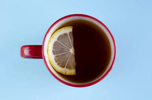 Czerwony kubek herbaty z cytryną w plasterkach kompozycji na niebieskim tle. — Zdjęcie stockowe