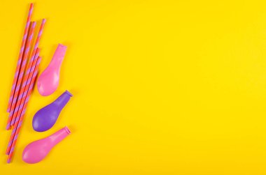 Sarı arka plan, parti ve kutlama dekorasyonunda renkli pipetler ve hava balonları kompozisyonu.