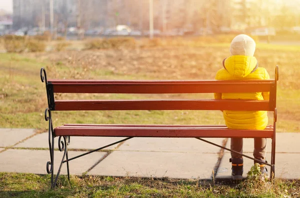 A gyerek egyedül ül a padon. Sárga kabátos fiú.. — Stock Fotó