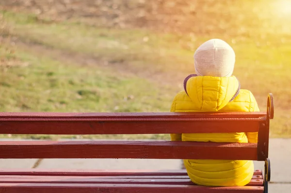 子供は一人で木のベンチに座っている。黄色のジャケットの男の子. — ストック写真