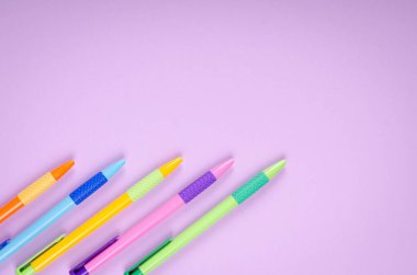 Farklı renkte kalemler, mor arkaplan kompozisyonu üzerine okul tükenmez kalemleri.