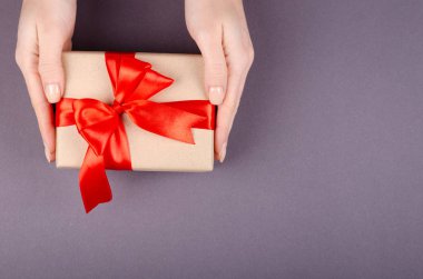 Koyu arkaplan kompozisyonu üzerinde hediye kutusu olan eller, kurdele ve yay ile mevcut..