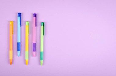 Farklı renkte kalemler, mor arkaplan kompozisyonu üzerine okul tükenmez kalemleri.
