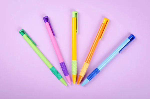 Bolígrafos de diferentes colores, bolígrafo escolar en la composición de fondo púrpura. — Foto de Stock
