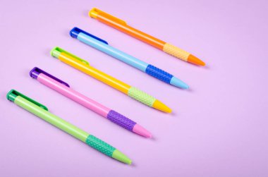 Farklı renkte kalemler, mor arka plan kompozisyonu üzerine okul tükenmez kalemleri. Düz konum ve fotokopi alanı ile üst görünüm fotoğrafı.