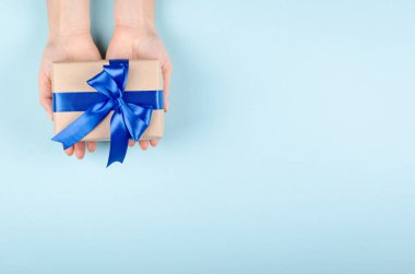 Hands with gift box on blue background composition, present with ribbon and bow. Flat lay and top view photo with copy space.