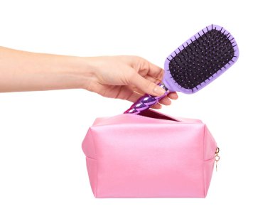 Elinde pembe makyaj çantası ve saç fırçası olan bir el. Cazibeli kozmetik aksesuar. Beyaz arkaplanda izole.