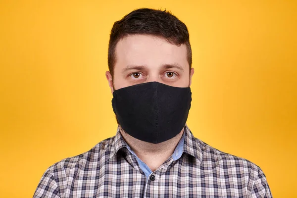Man in black face mask looking at camera, isolated on orange background. Coronavirus concept.