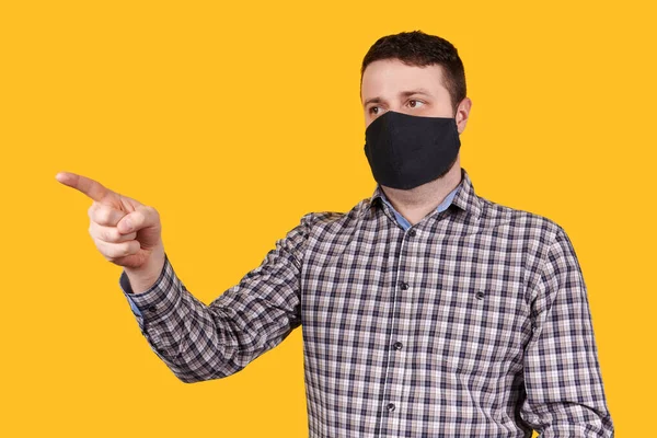 黒い顔のマスクを指で指している男は オレンジの背景に隔離された コロナウイルスの概念 — ストック写真