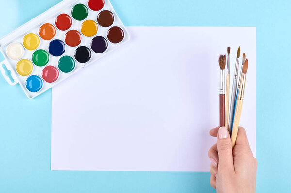 Рука с акварелью краски и кисти на синем фоне. Плоское положение, вид сверху. Копирование пространства, шаблон
.