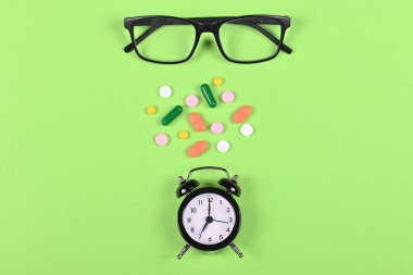 Tıbbi haplar, gözlükler ve saat yeşil arka plan, düz yatış, yukarıdan görüntü. Uyuşturucu konseptini kullanma zamanı.
