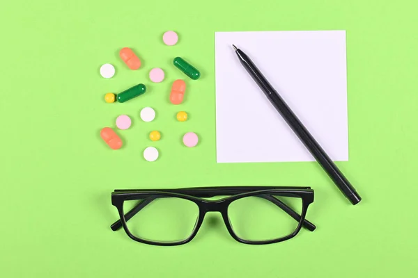 Medical pills, recipe and glasses on green background, flat lay, overhead view image.