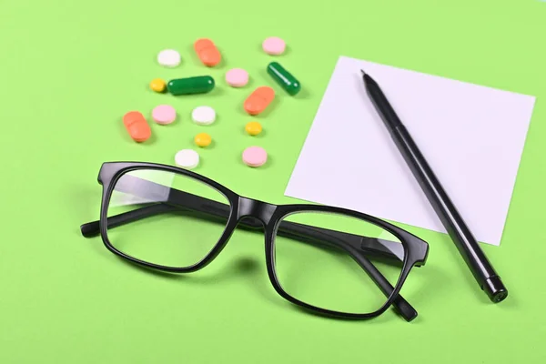 Medical pills, recipe and glasses on green background, flat lay, overhead view image.