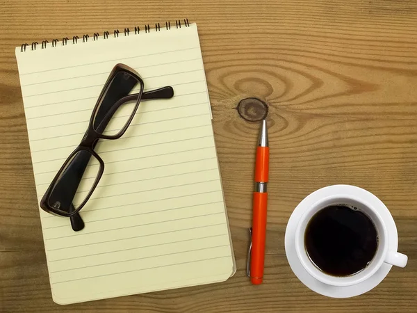Σημειωματάριο, γυαλιά, στυλό και φλιτζάνι καφέ σε ξύλινο φόντο. — Φωτογραφία Αρχείου