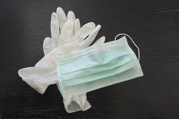 Medical protective mask and white latex gloves over black wooden background.