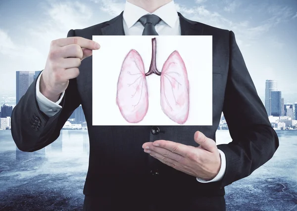 Empresario sosteniendo y mostrando una tarjeta con un dibujo de pulmones sanos en el fondo de la ciudad. Concepto de salud —  Fotos de Stock
