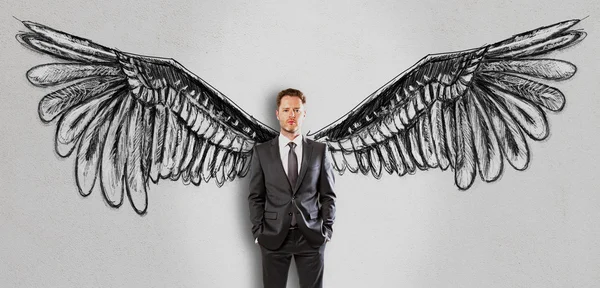 Gutaussehender Geschäftsmann im Anzug auf Betongrund mit kreativ gezeichneten Flügeln. Freiheitskonzept — Stockfoto