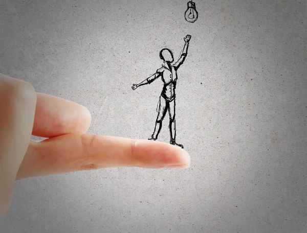 Close up of finger holding abstract sketch of little human trying to reach light bulb on concrete backgroud. Conceito de ideia — Fotografia de Stock