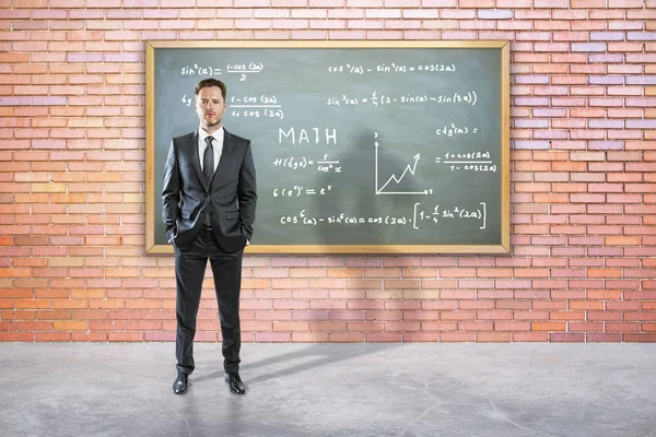Красивый молодой бизнесмен в костюме противостоит доске с математическими формулами. Концепция образования — стоковое фото