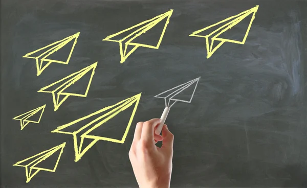 Male hand drawing paper plane sketches on chalkboard background. Leadership concept