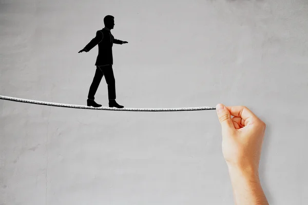 Silueta de hombre de negocios dibujado caminando sobre una cuerda que está siendo sostenida por la mano masculina. Fondo del concierto. Concepto de equilibrio —  Fotos de Stock