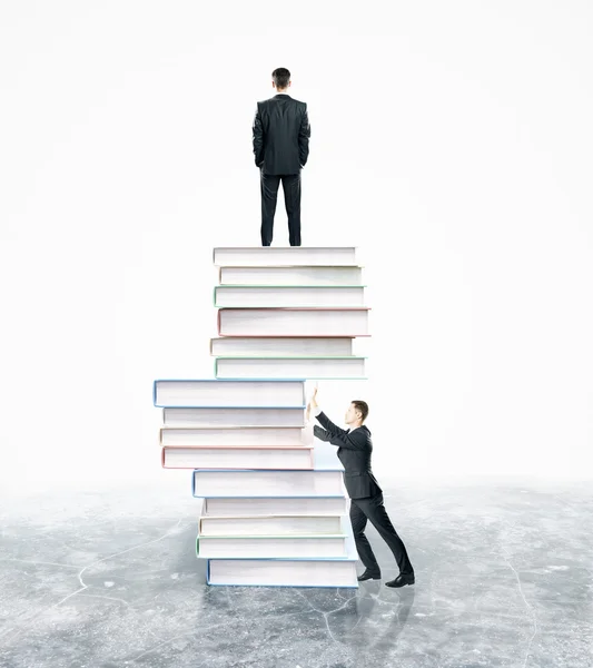 Des hommes d'affaires debout et poussant une pile abstraite de livres sur fond blanc. Concept de concurrence — Photo