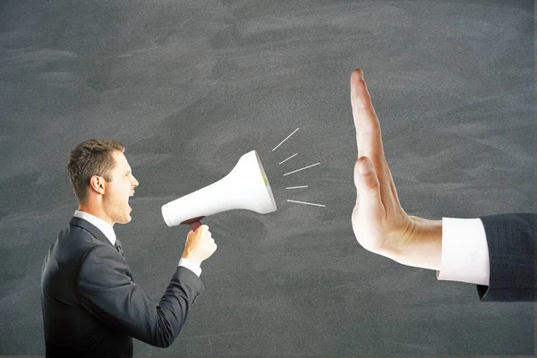 Irritated young businessman with megaphone screaming at hand showing stop gesture on chalkboard background. Protest concept — Stock Photo, Image