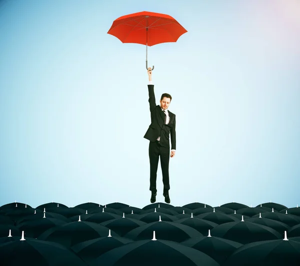 Joven hombre de negocios con paraguas rojo volando sobre paraguas negros sobre fondo azul. Concepto de liderazgo. Renderizado 3D — Foto de Stock