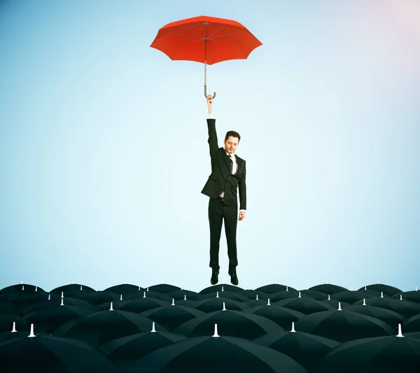 Young businessman with red umbrella flying above black umbrellas on blue background. Leadership concept. 3D Rendering — Stock Photo, Image