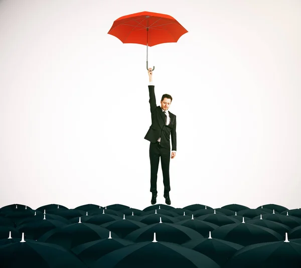 Joven hombre de negocios con paraguas rojo volando sobre paraguas negros sobre fondo claro. Concepto de liderazgo. Renderizado 3D — Foto de Stock
