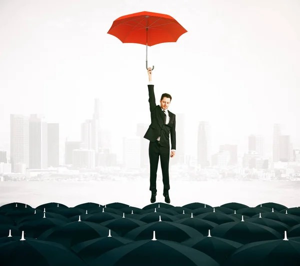 Joven hombre de negocios con paraguas rojo volando por encima de paraguas negros en el fondo de la ciudad. Concepto de liderazgo. Renderizado 3D — Foto de Stock