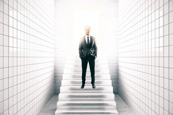 Vista frontal do jovem empresário em azulejo branco interior em pé sobre escadas. Conceito de sucesso. Renderização 3D — Fotografia de Stock