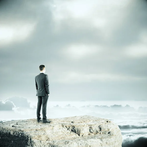 Homme d'affaires réfléchi debout sur une falaise et regardant au loin. Fond ciel terne. Concept de recherche — Photo