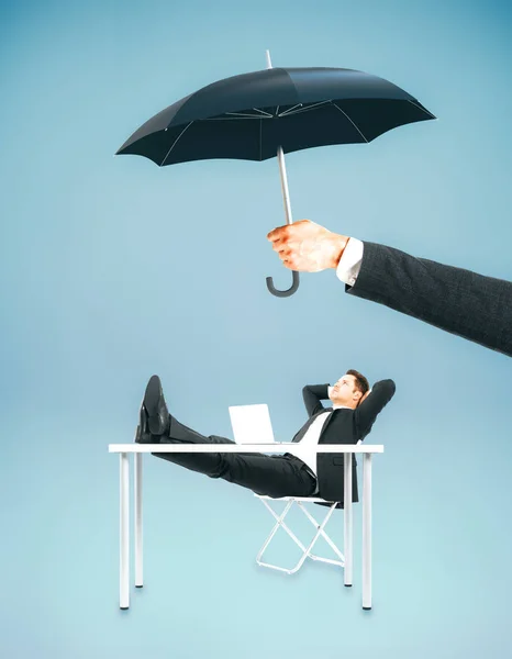 Hand hält Regenschirm über Geschäftsmann entspannt am Arbeitsplatz. Sicherheitskonzept. blauer Hintergrund — Stockfoto