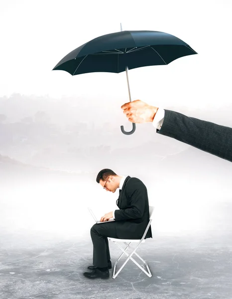 Hand holding umbrella over working businessman. Protection concept. Landscape background Stock Photo